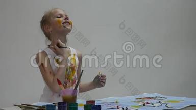 可爱的小女孩画家在桌子上画画，在她的衣服上画画。 慢动作